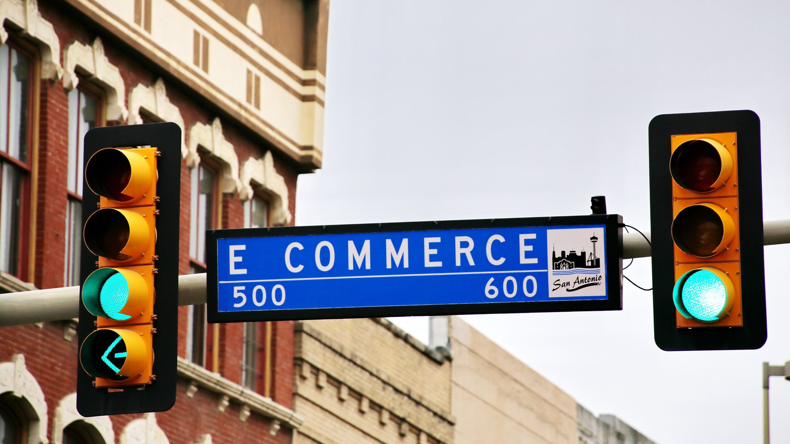 a street sign suspended between two stoplights reads "E commerce"